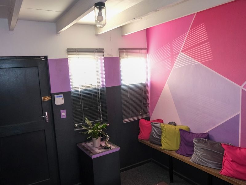 A functional office space featuring exposed ceiling beams, built-in bench seating, and venetian blinds, finished with a bold geometric wall paint design.