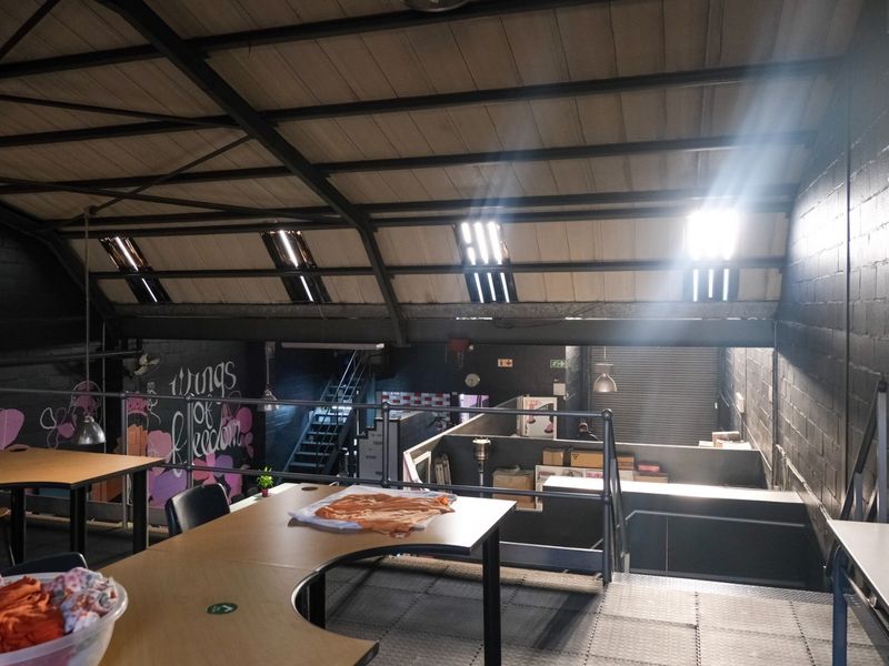 Industrial mezzanine office space featuring exposed steel roof trusses, skylights, and a metal floor, overlooking the main warehouse area.