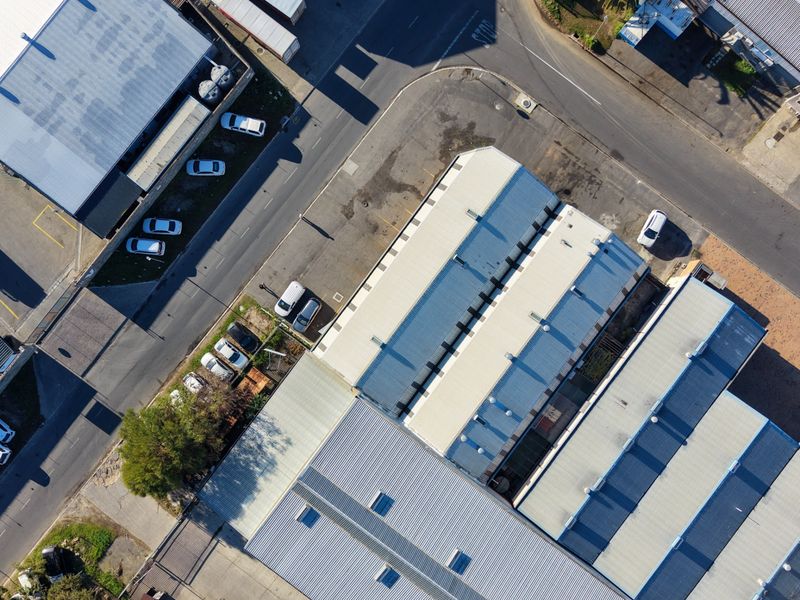 Aerial view of an industrial property complex featuring multiple warehouse units with metal roofing, skylights, and an adjacent asphalt parking area.