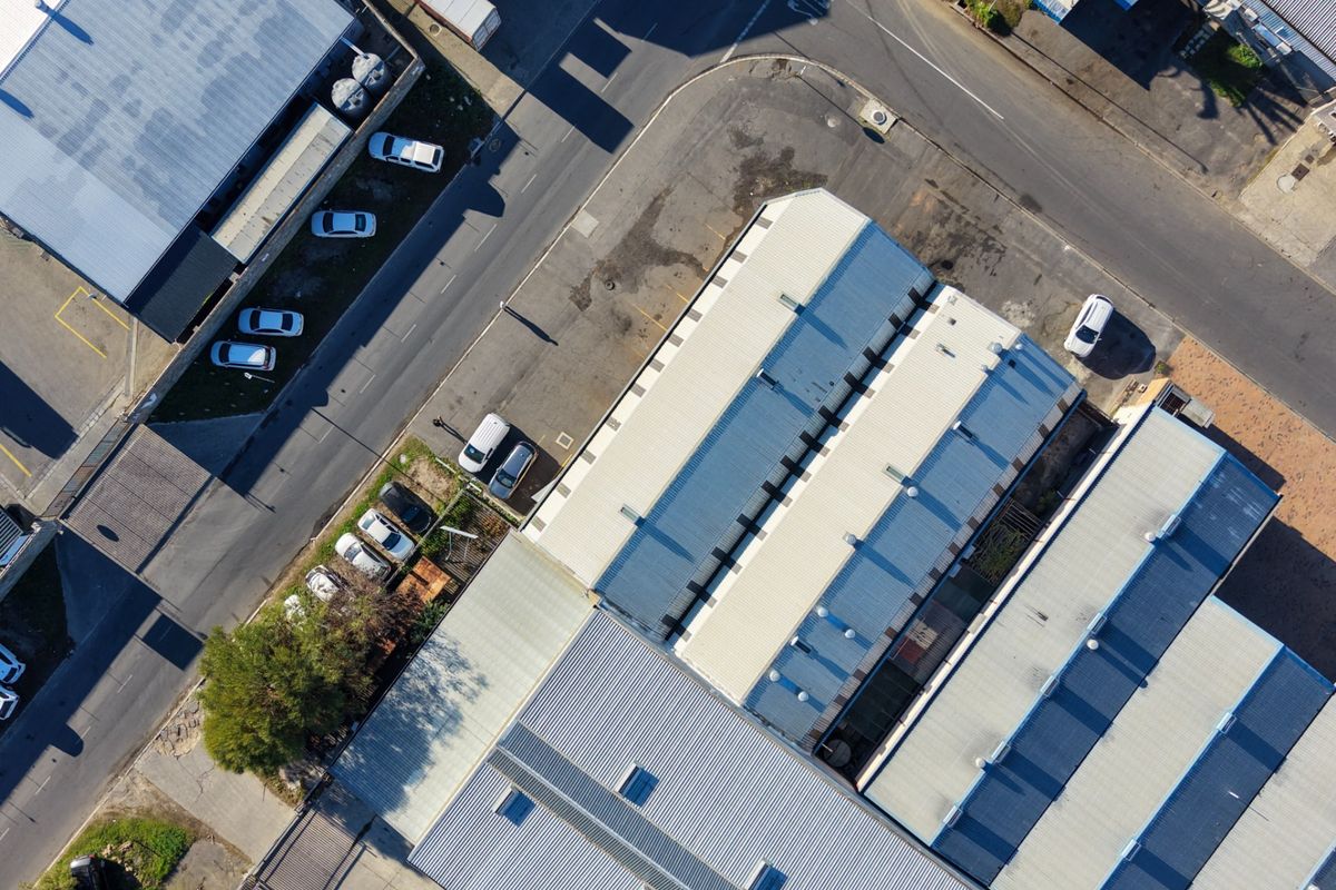 Aerial view of an industrial property complex featuring multiple warehouse units with metal roofing, skylights, and an adjacent asphalt parking area.