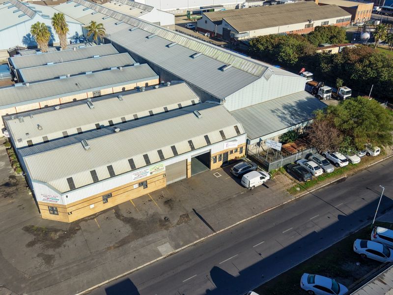 Aerial view of an industrial warehouse complex featuring corrugated metal roofing, brick facade, and dedicated paved parking area with security fencing.