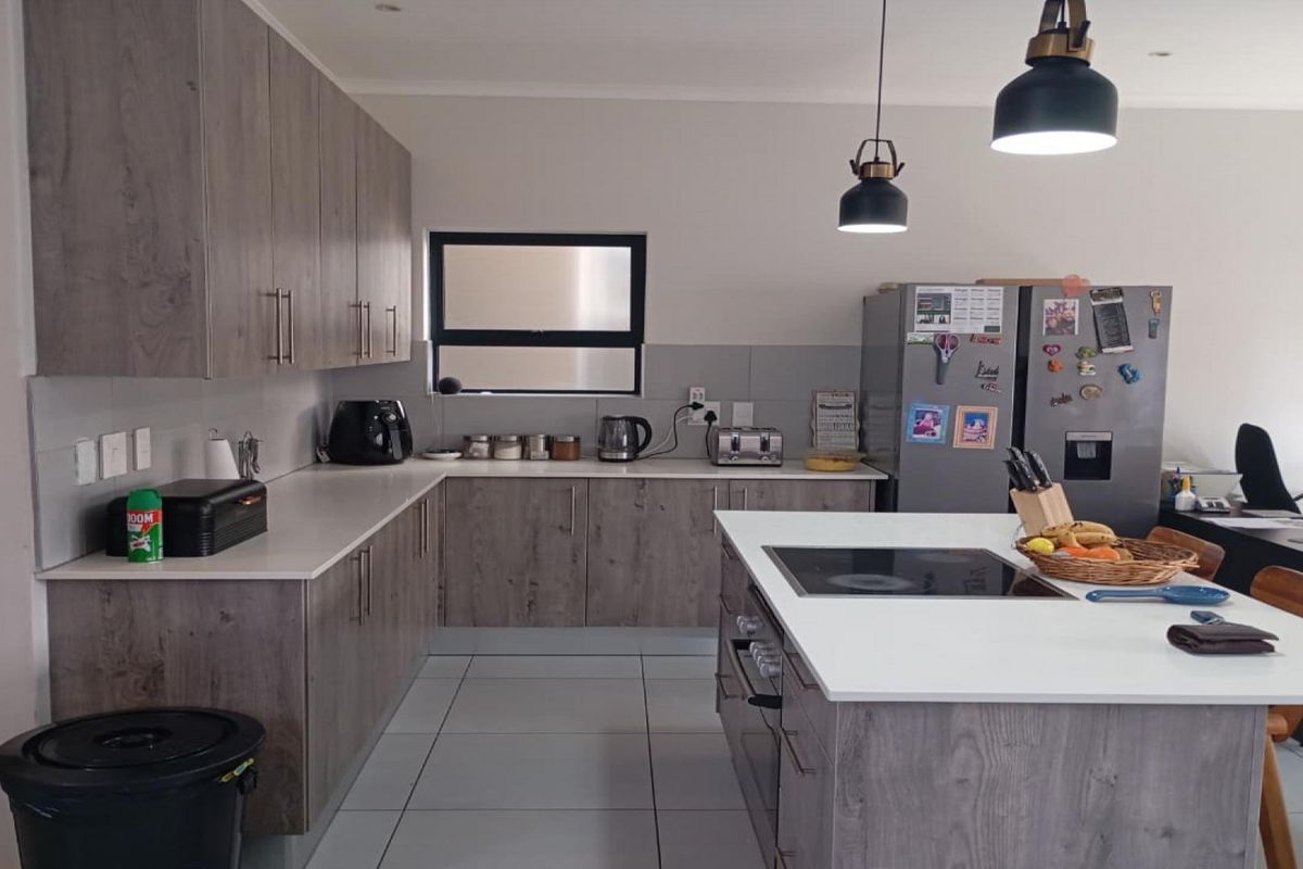 Modern kitchen featuring wood-look cabinetry, stone countertops, a central island with a built-in cooktop, and tiled flooring.