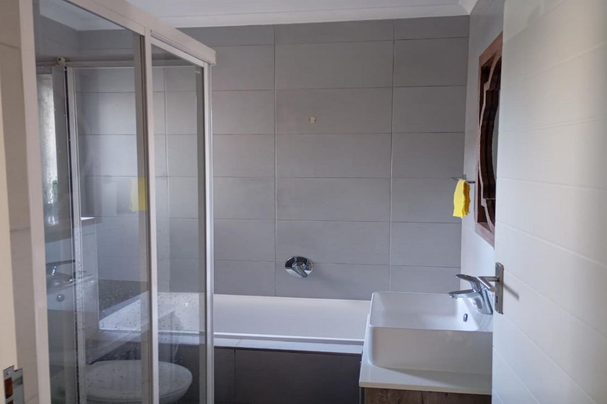 A functional bathroom featuring a glass shower enclosure, a built-in bathtub with wall-mounted mixer, and a modern vanity basin with tiled wall finishes.