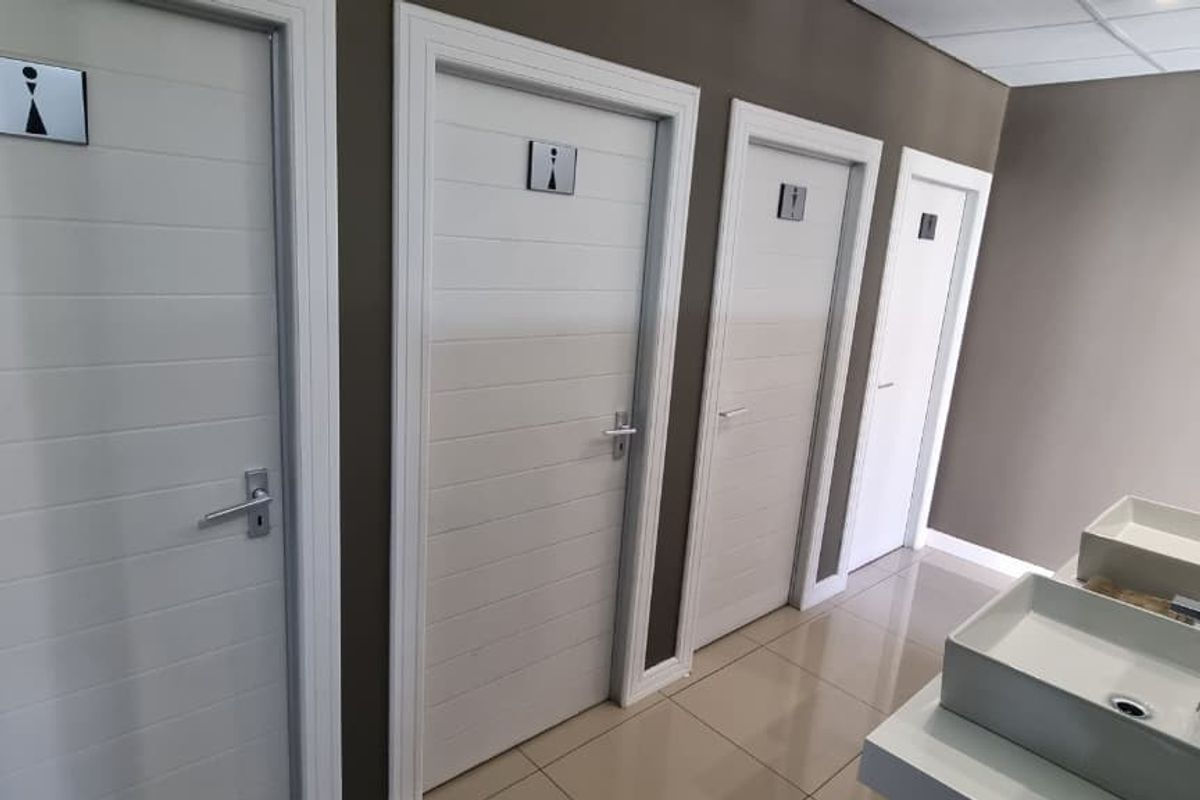 Modern office restroom facility featuring multiple stalls, tiled flooring, and a clean vanity area with vessel sinks.