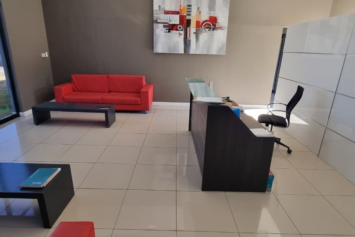 A modern office reception area featuring tiled flooring, a built-in reception desk, and large glass doors providing natural light.
