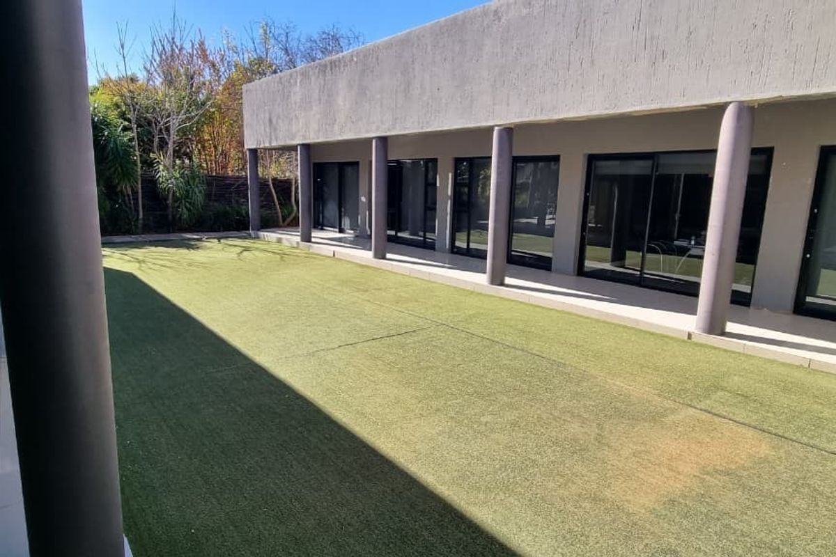 Rear exterior view of the office building featuring a covered patio with tiled flooring, concrete columns, and an artificial turf lawn area.