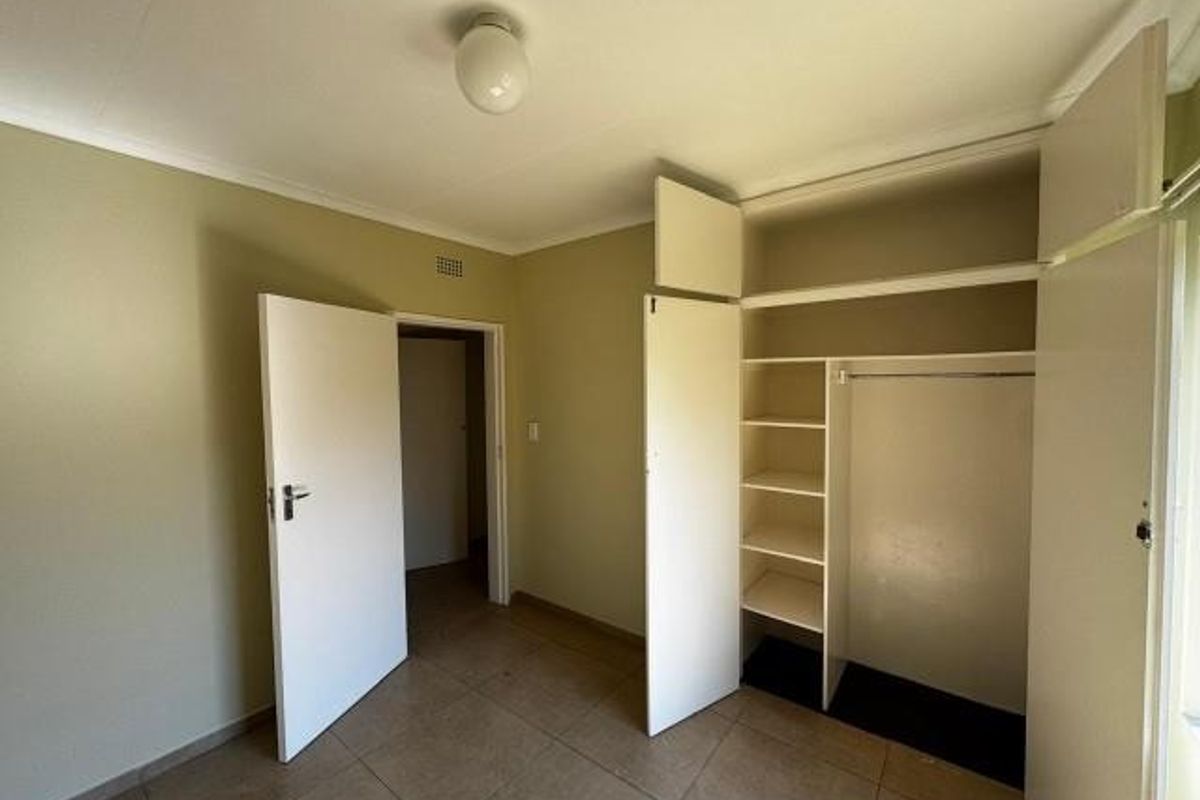 A clean, empty bedroom featuring neutral wall tones, tiled flooring, and a functional built-in wardrobe with shelving and hanging space.