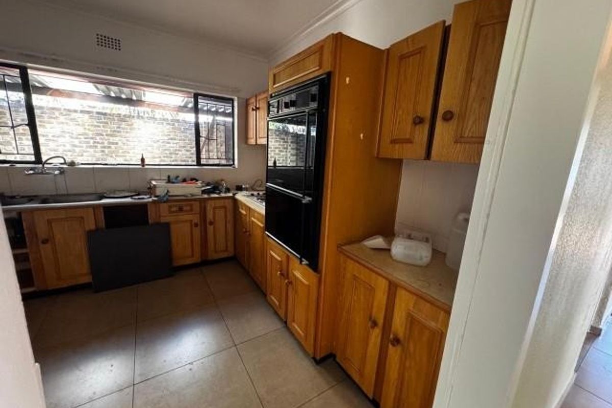 A functional kitchen featuring wooden cabinetry, a built-in double oven, and tiled flooring, offering potential for a modern renovation.