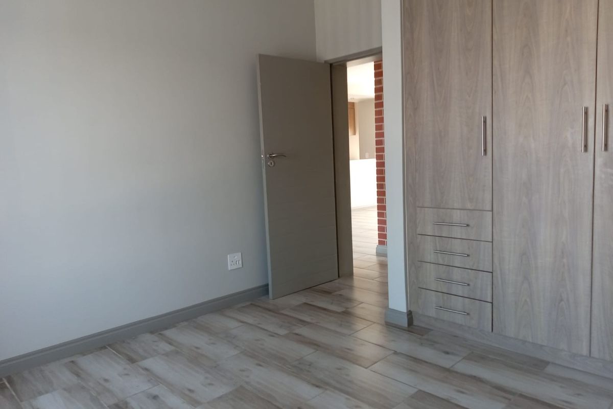 A clean, empty bedroom featuring modern wood-look tiled flooring and built-in cupboards with integrated drawers, offering a neutral and well-maintained living space.