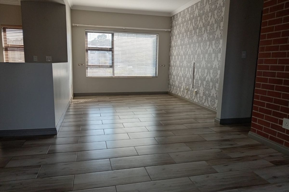 An empty living room featuring wood-look tiled flooring, a decorative feature wall, and an exposed brick accent, offering a clean and versatile living space.