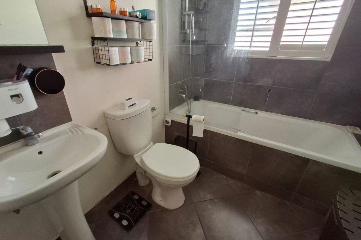 A functional bathroom featuring a pedestal basin, toilet, and a bathtub with a glass shower screen and tiled finishes.