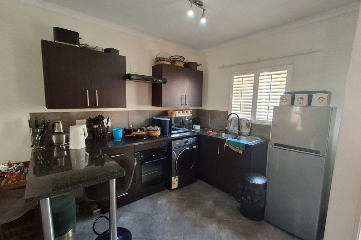 A functional kitchen featuring dark wood cabinetry, granite countertops, built-in oven, extractor fan, and tiled flooring with integrated laundry space.