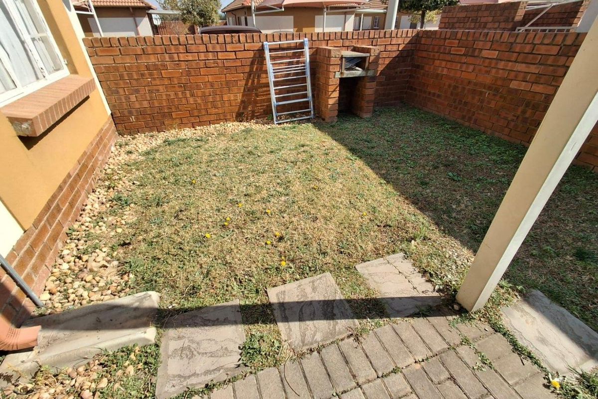 A private rear courtyard featuring a paved patio, a built-in brick braai, and a small garden area enclosed by brick boundary walls.