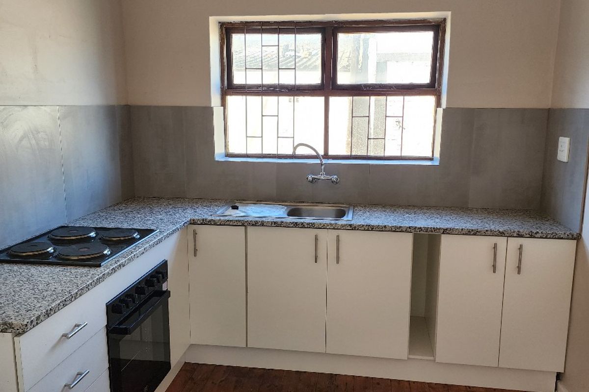 A functional kitchen featuring white cabinetry, granite countertops, built-in oven, electric hob, and timber flooring, offering a clean and practical workspace.