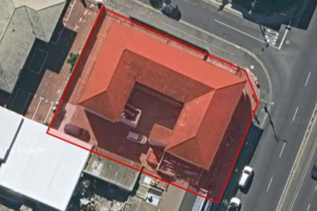 Aerial view of a commercial property featuring a U-shaped building layout with a tiled roof, situated on a corner lot.