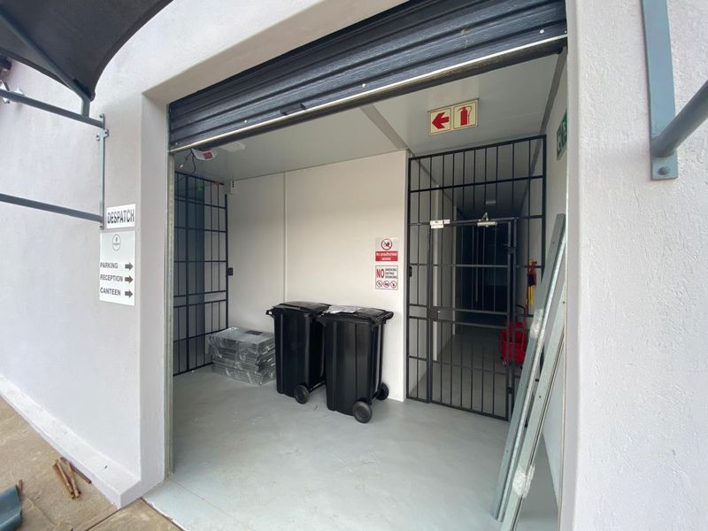 A secure utility or dispatch area featuring a roller shutter door, security gate, and durable epoxy flooring, suitable for industrial or commercial storage use.