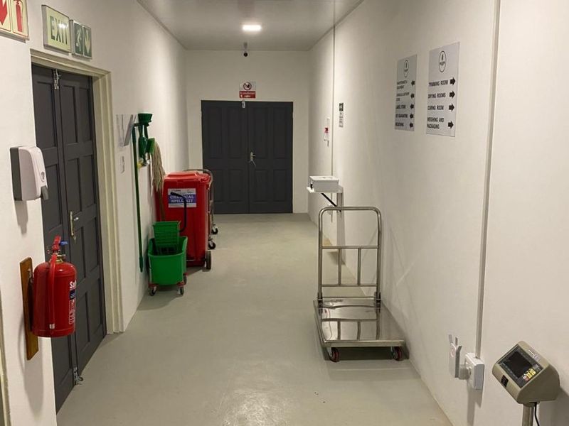 A clean, functional industrial hallway featuring emergency signage, fire safety equipment, and durable flooring, providing access to various facility rooms.