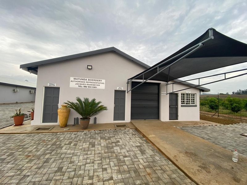 Front view of a farm facility building featuring paved driveway, shade sail, roller shutter door, and designated male and female ablution entrances.