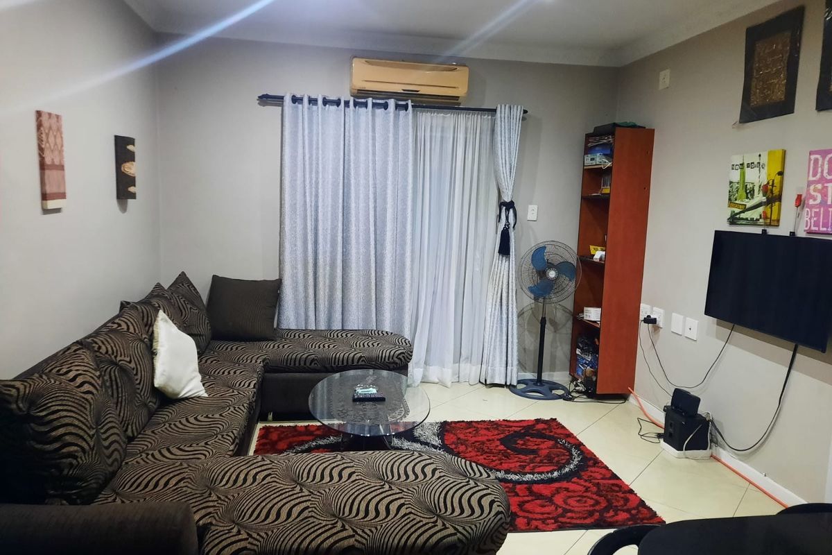 A living room featuring tiled flooring, recessed downlighting, and a wall-mounted air conditioning unit with access to a patio or balcony area.