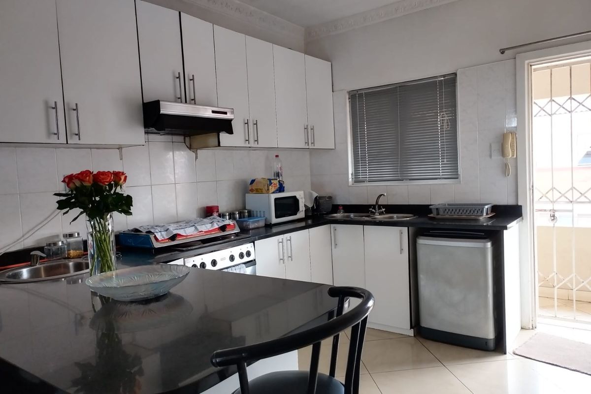 Functional kitchen featuring white cabinetry, black granite countertops, built-in stove, extractor fan, and direct access to an outdoor balcony area.