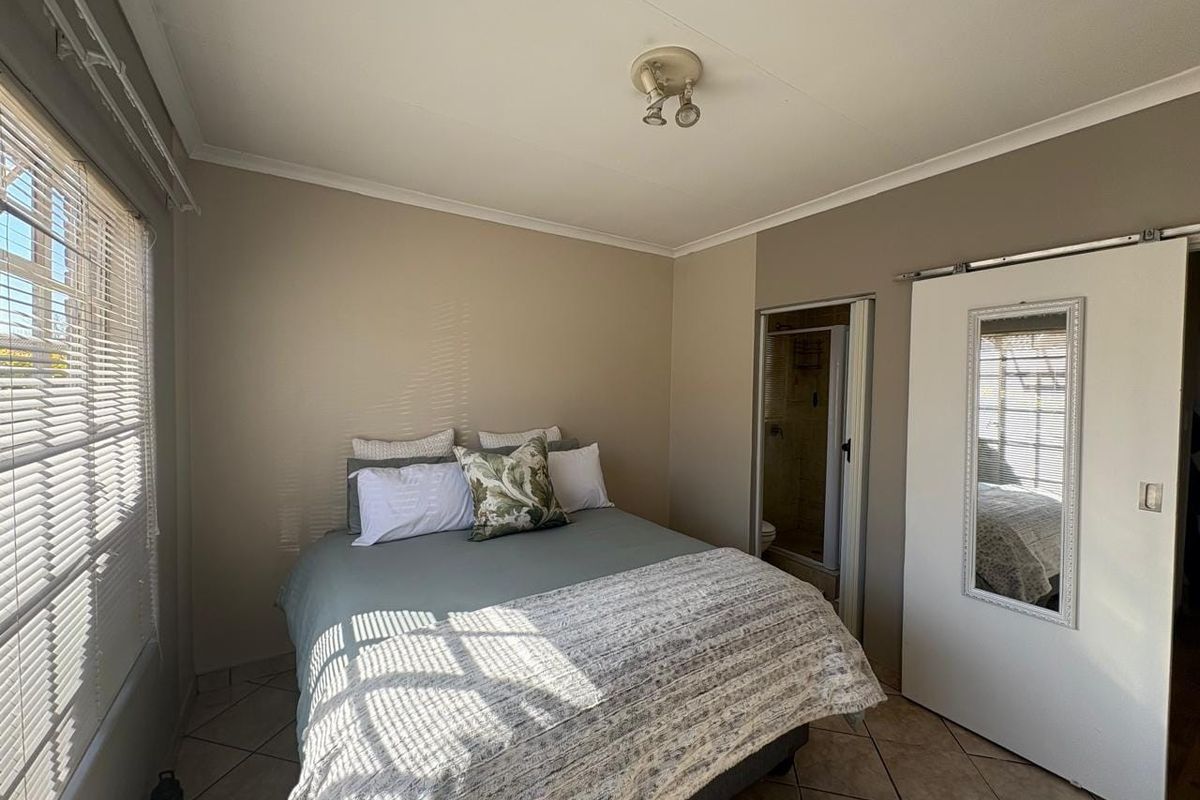 A functional bedroom featuring tiled flooring, a sliding door leading to an en-suite bathroom, and neutral wall tones.