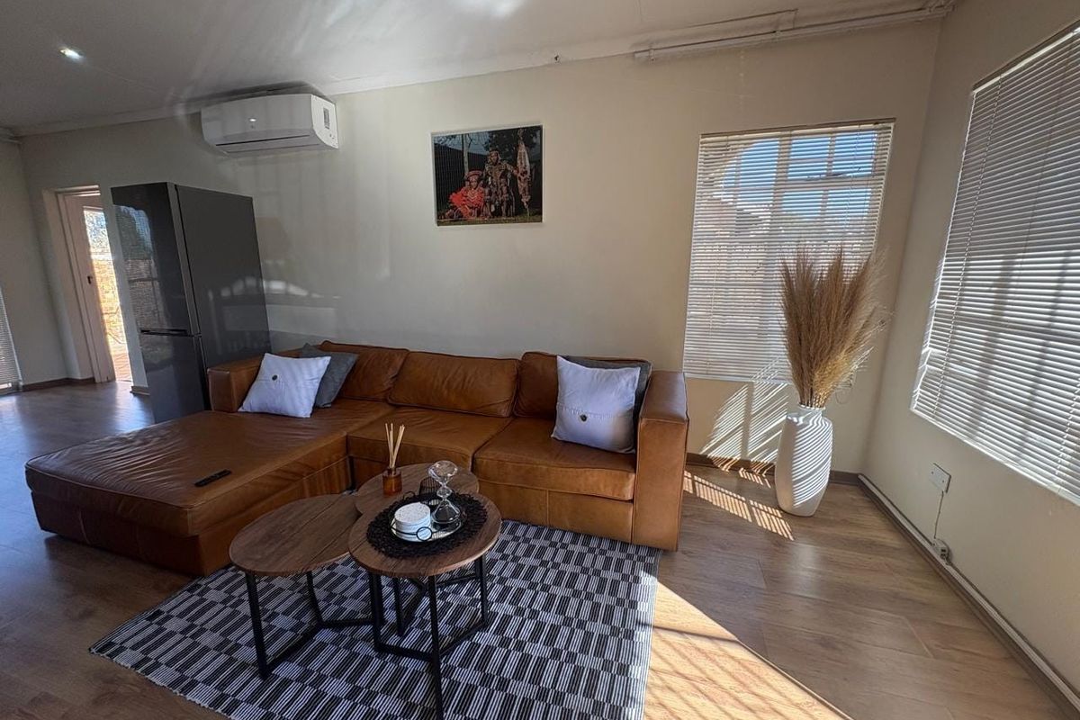 A bright living room featuring laminate flooring, recessed downlighting, and a wall-mounted split-system air conditioner, offering a comfortable and functional living space.