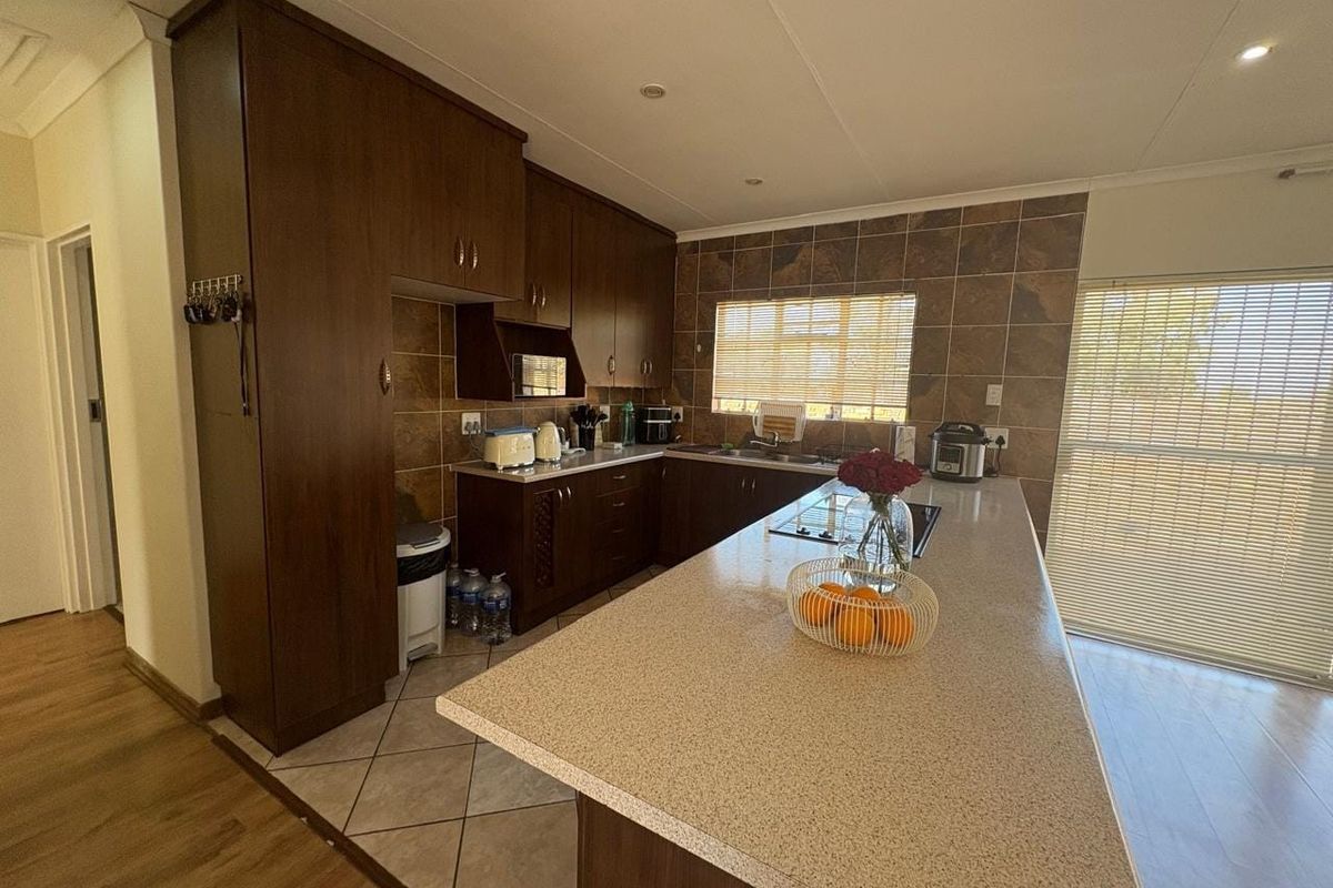 A functional kitchen featuring dark wood cabinetry, stone-look countertops, a central island, and tiled backsplash with integrated hob and sink.