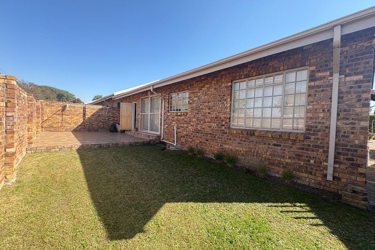 Rear view of the townhouse featuring a face brick facade, a paved patio area, and a private lawn enclosed by a boundary wall.