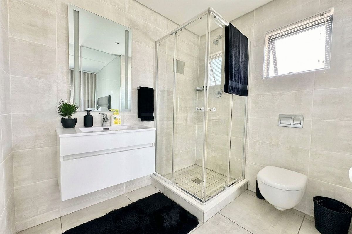 Modern bathroom featuring a wall-mounted vanity, glass shower enclosure, and wall-hung toilet with neutral floor-to-ceiling tiling.