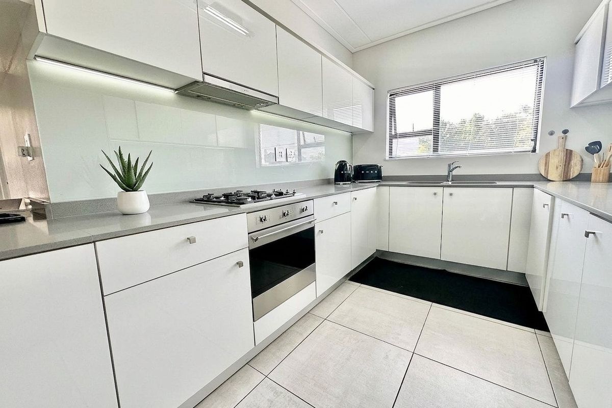 Modern kitchen featuring white high-gloss cabinetry, stone countertops, a gas hob, built-in oven, and a glass splashback with neutral tiled flooring.