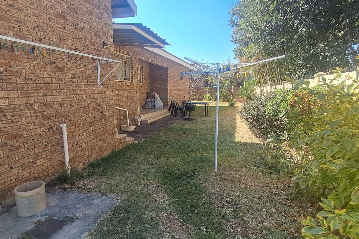 A rear garden view featuring a face brick exterior, a paved patio area, and a rotary clothesline set within a private backyard space.