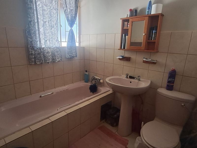 A functional bathroom featuring a built-in bathtub, pedestal sink, toilet, and wall-mounted medicine cabinet with neutral ceramic wall tiling.