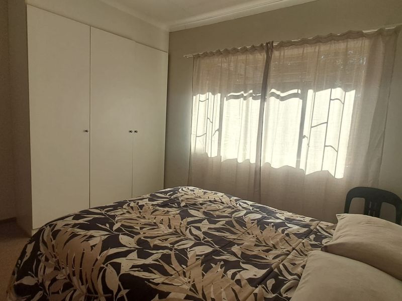 A bedroom featuring a built-in wardrobe and natural light through window curtains.