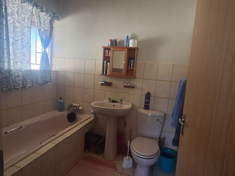 A functional bathroom featuring a pedestal basin, toilet, and bathtub with tiled walls and flooring, offering potential for modernization.