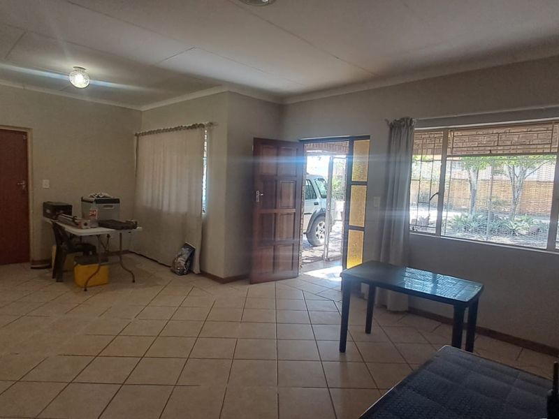 A spacious, open-plan living area featuring neutral tiled flooring, large windows for natural light, and direct access to the exterior.