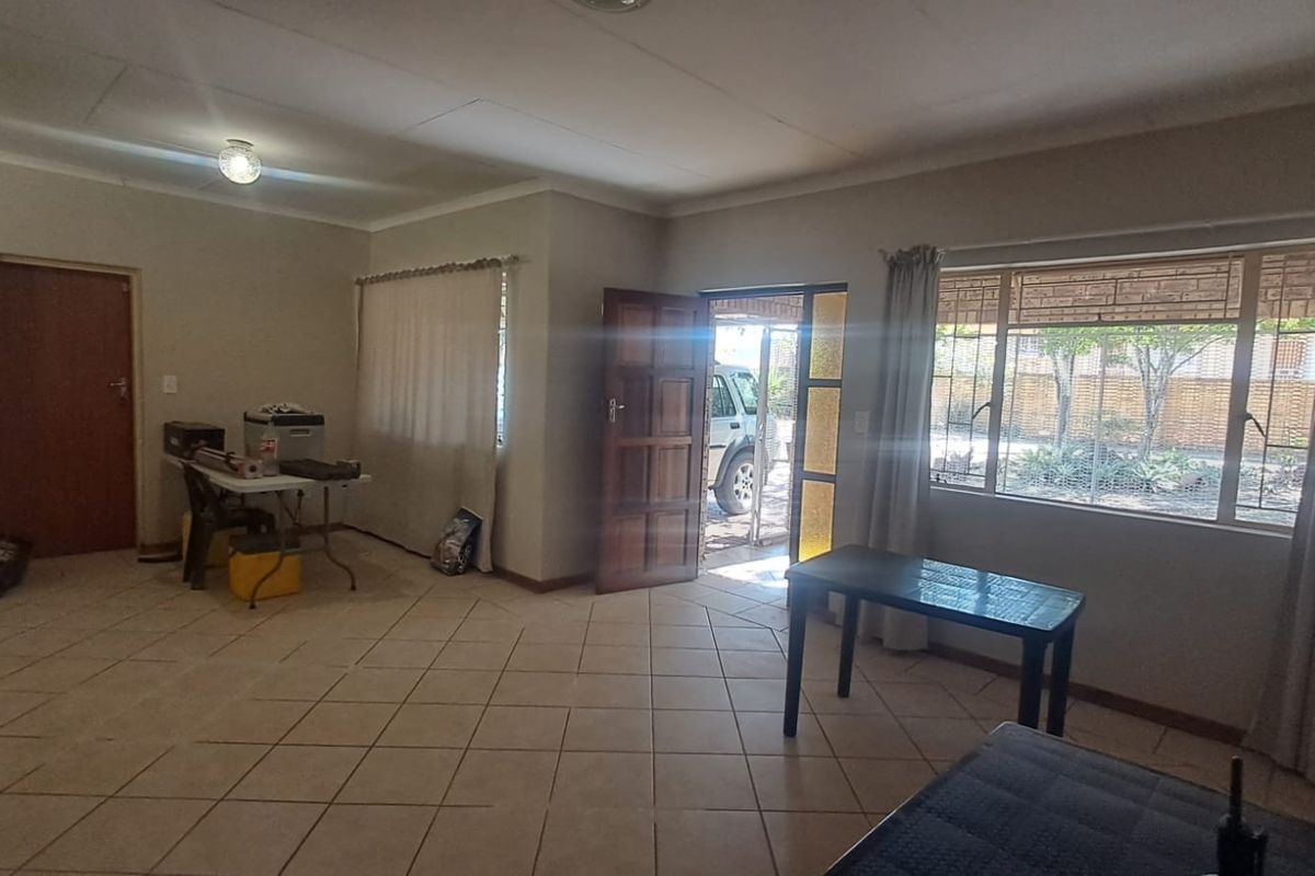 A spacious, open-plan living area featuring neutral tiled flooring, large windows for natural light, and direct access to the exterior.