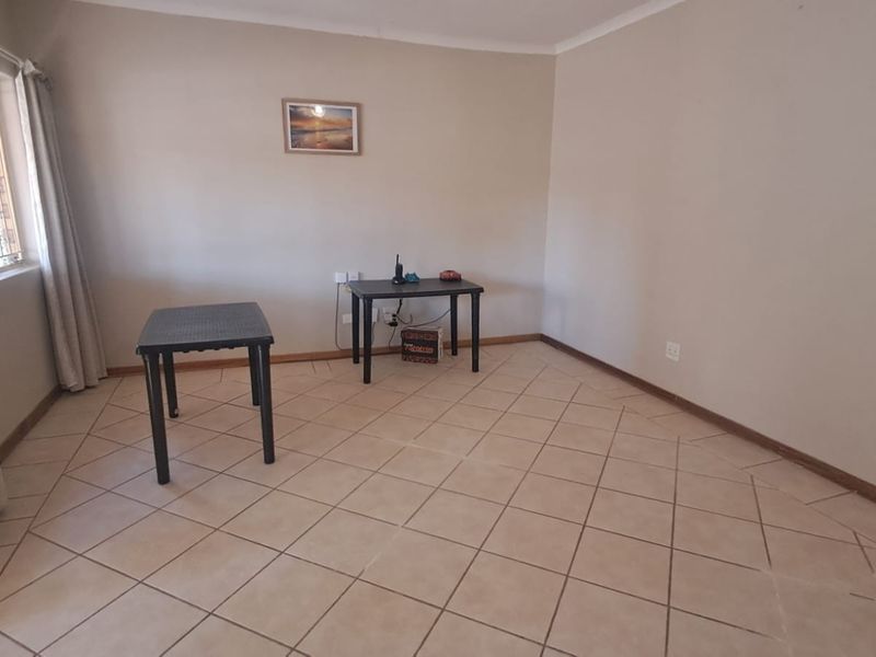 A spacious, neutrally painted living area featuring tiled flooring and cove cornicing, offering a blank canvas for interior design.