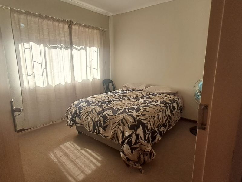 A standard bedroom featuring carpeted flooring and natural light through window curtains.