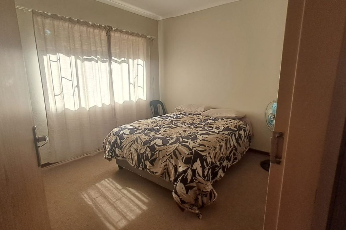 A standard bedroom featuring carpeted flooring and natural light through window curtains.