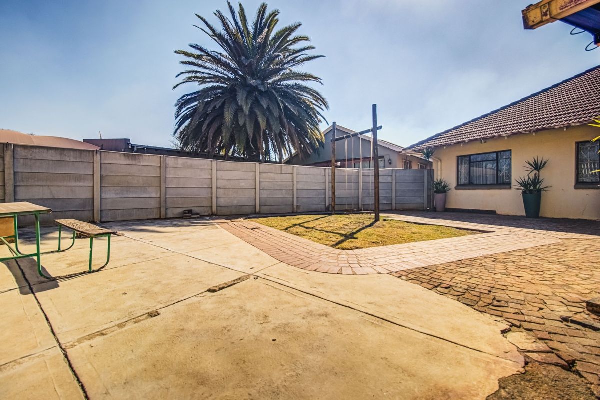 Rear garden area featuring a paved patio, precast concrete boundary wall, and a small lawn section with a swing set.