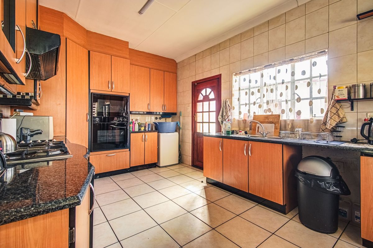 A functional kitchen featuring wood-finish cabinetry, granite countertops, a built-in oven, gas hob, and tiled flooring with direct access to the exterior.