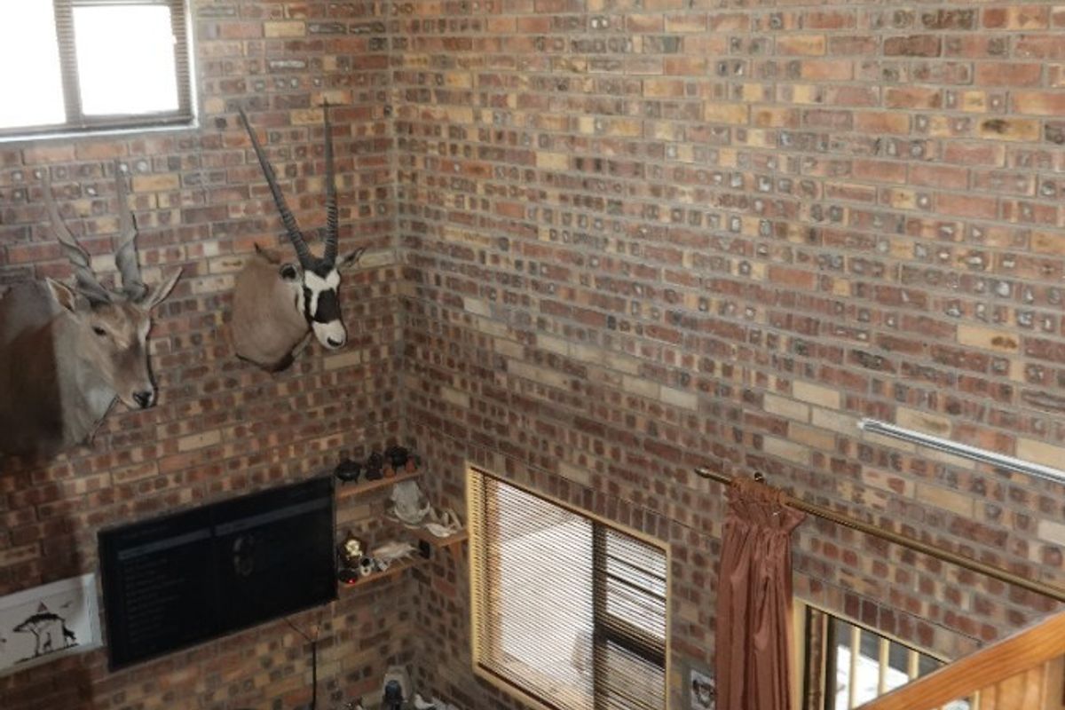 A double-volume living area featuring exposed brick walls, high vaulted ceilings, and a timber staircase with a wooden balustrade.