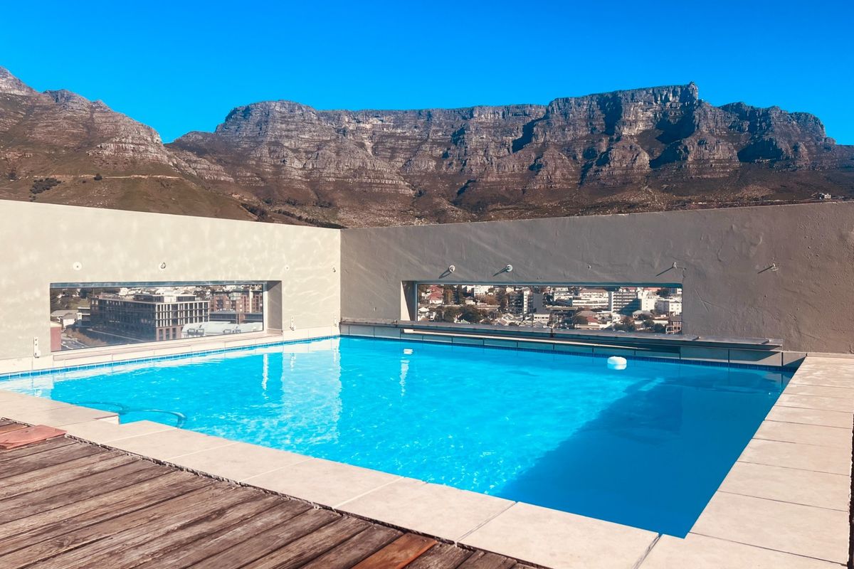 Rooftop swimming pool featuring timber decking, stone coping, and concrete parapet walls with integrated apertures offering panoramic mountain and city views.