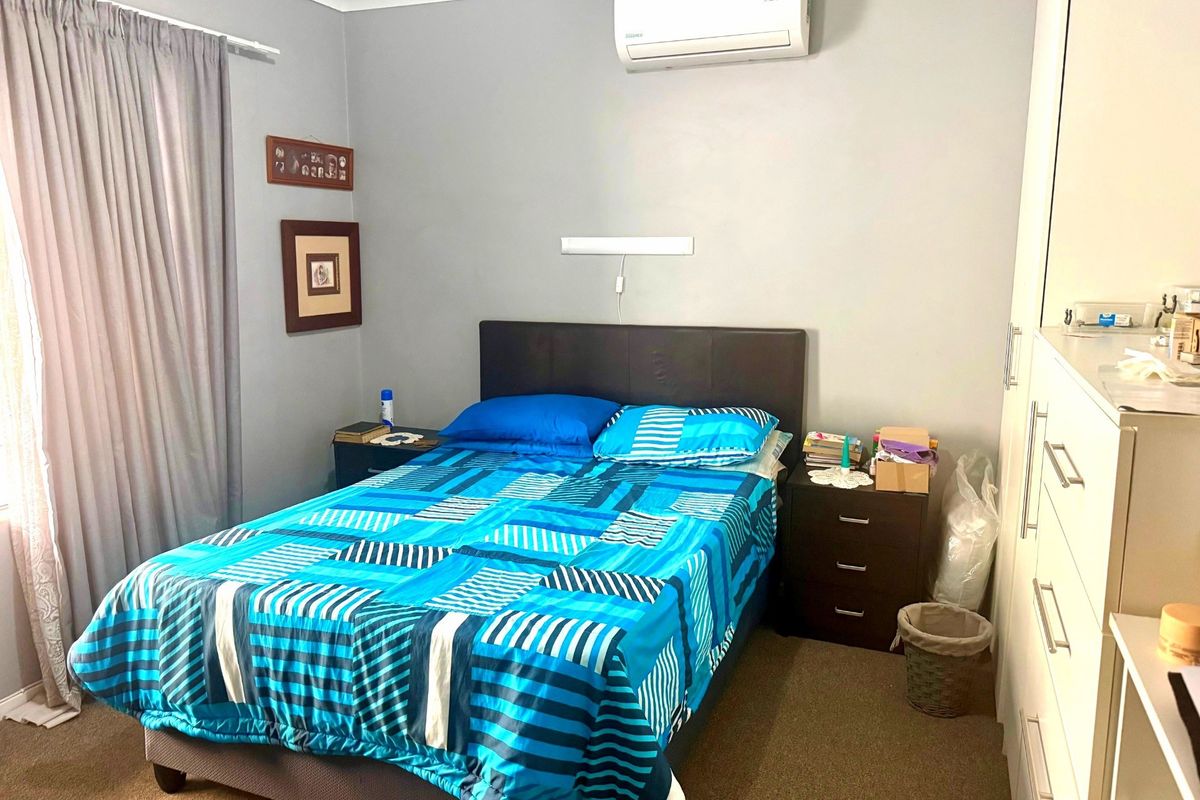 A functional bedroom featuring carpet flooring, a wall-mounted split-system air conditioner, and built-in wardrobe storage.