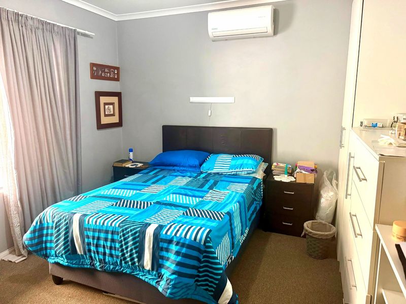 A functional bedroom featuring carpet flooring, a wall-mounted split-system air conditioner, and built-in wardrobe storage.