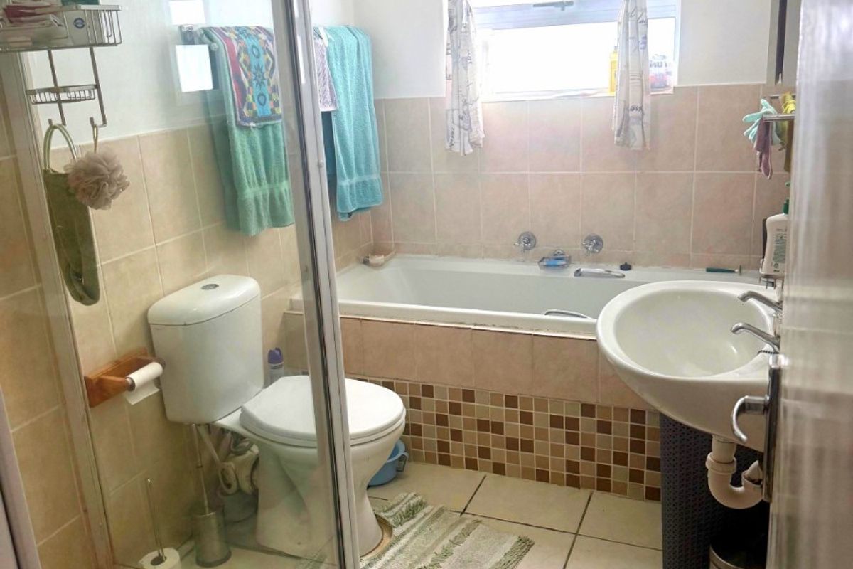 A functional bathroom featuring a shower enclosure, bathtub, pedestal basin, and toilet with neutral wall and floor tiling.