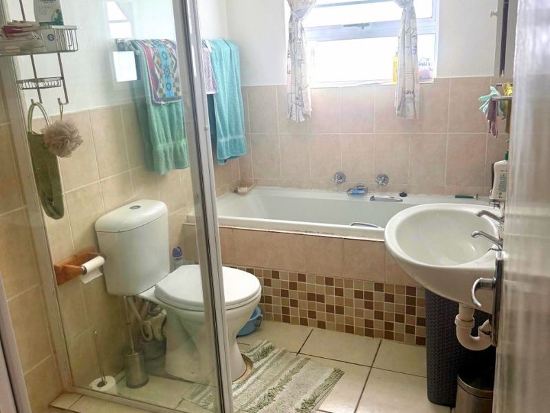 A functional bathroom featuring a shower enclosure, bathtub, pedestal basin, and toilet with neutral wall and floor tiling.