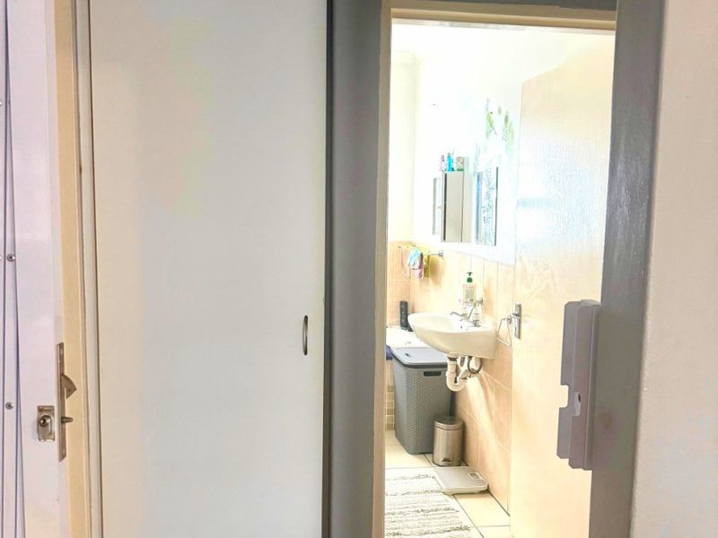 A view from a hallway looking into a bathroom featuring a pedestal basin and tiled finishes, with an adjacent built-in cupboard.