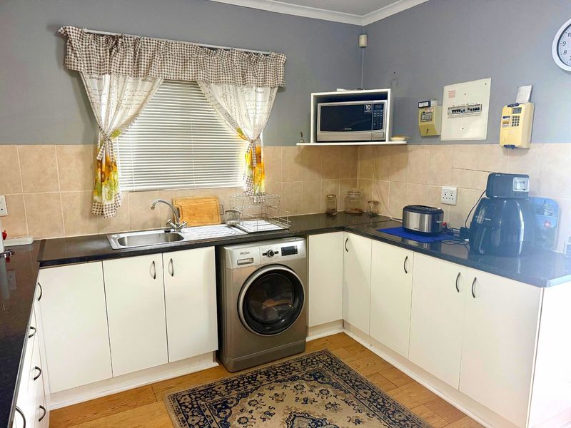 A functional kitchen featuring white cabinetry, dark laminate countertops, tiled backsplash, and a dedicated space for laundry appliances.