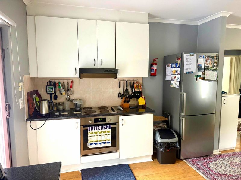 A functional kitchen featuring white cabinetry, a built-in oven with electric cooktop, extractor fan, and tiled backsplash, providing a practical cooking space.